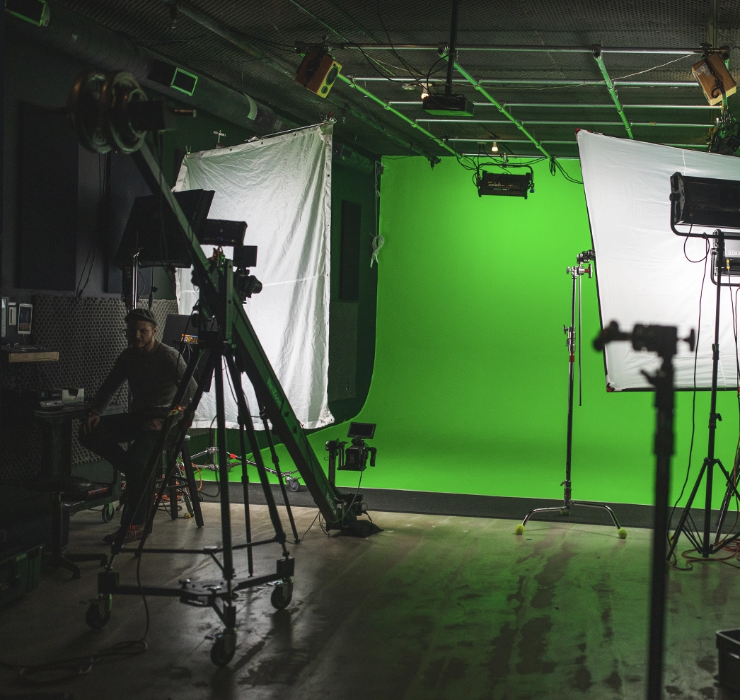 A man sits at the side of a professional video production set, surrounded by lights and equipment during a video production shoot.