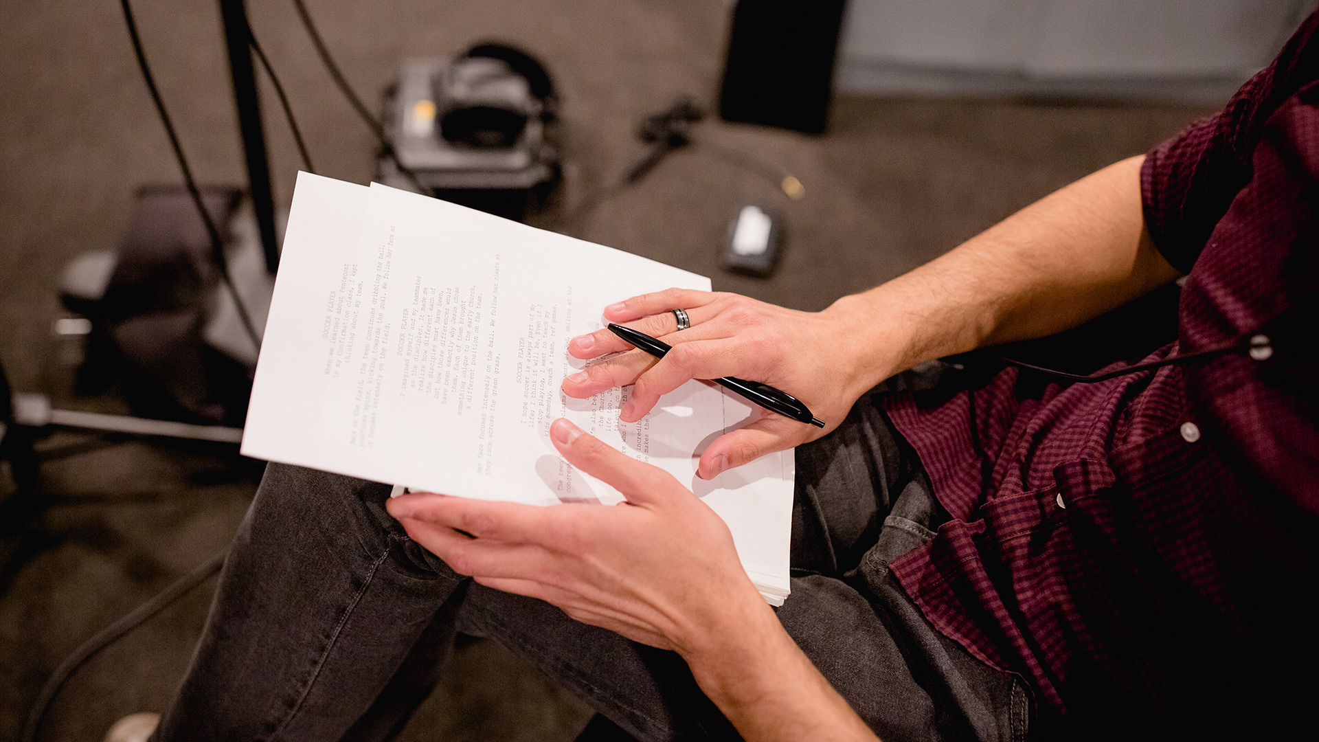 A filmmaker reviews a printed script while holding a pen on set, representing the refining stage in how to script a commercial video.