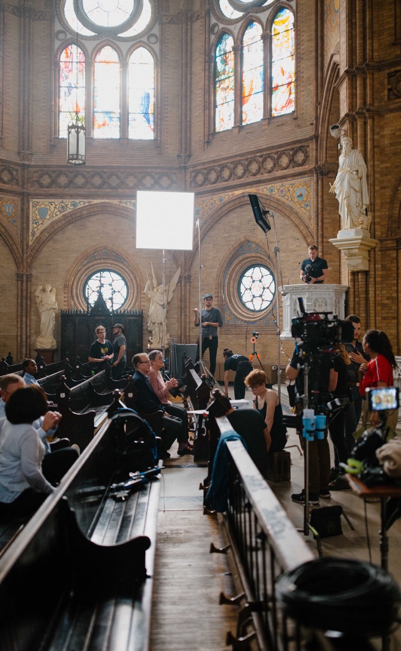 A Catholic video production crew films inside a church with lighting, cameras, and cast in place, showing how production complexity which affects video production cost vs value and why a higher video production cost does not always mean a better video.